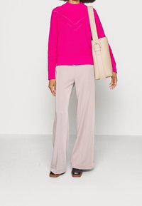 Pull en tricot rose vif avec un col montant et un motif en chevrons ; pantalon large beige ; sac à épaule beige clair ; chaussures marron foncé.