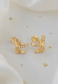 Guldörhängen med en skulptural design och klara rhinestones som accenterar kurvan, mot en mjuk, ljus bakgrund.