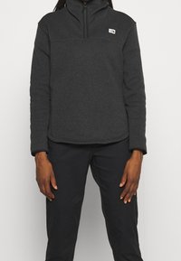 Dunkelgrauer Pulloverjacke aus Fleece, mit hohem Kragen, halblanger Reißverschlussöffnung und kleinem Logo auf der oberen linken Brust.