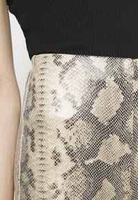Skinnmönstrad kjol i ljus beige och mörkbruna toner; texturerad, slät yta med resårmidja och ribbad svart topp.