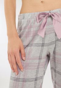 Primo piano della vita e della mano di una donna che indossa pantaloni a quadretti grigi con un fiocco di raso viola chiaro legato in vita.