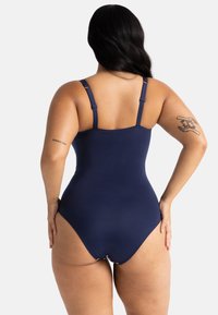 Tumedast sinise värvi üheosalise ujumiskostüümi reguleeritavad rihmad, sile tekstuur ja mõõdukas katvus, millel on madala lõikega seljaosa disain ja diskreetne logo detail.