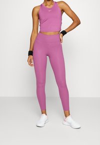 Roze sportieve crop top met een gouden logo, gecombineerd met bijpassende high-waisted leggings. Witte sportschoenen maken de outfit compleet.