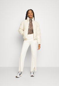 Cream puffer jacket with high collar, animal print mock neck, white split-hem pants, and multicolored sneakers. Casual outfit ensemble.