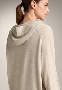 Beige hoodie met een zachte textuur, een relaxte pasvorm en een eenvoudig ontwerp. De capuchon is bevestigd aan de achterkant van de halslijn.