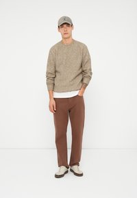 Khaki knit sweater with a textured pattern, brown straight-leg pants, and beige sneakers. Cap is light gray with a subtle logo.