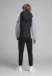 Svart och grå vadderad jacka med huva, med en delad design. Kombinerad med svarta cargobyxor och vita ankel sneakers.