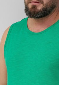 Zielona bezrękawnik z teksturowanej tkaniny, z okrągłym dekoltem i małym haftowanym logo na piersi.