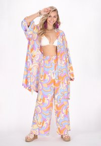 Costum de plajă multicolor, care include un kimono cu model, un bikini alb și pantaloni wide-leg asortați, cu șnur. Materialul pare ușor.