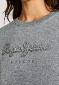Sudadera gris con cuello redondo. Presenta un logotipo texturizado y brillante de "Pepe Jeans" en letras cursivas y mayúsculas, con "LONDON" debajo.