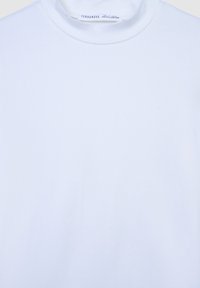 T-shirt bianco in cotone con collo alto, tessuto liscio e design minimalista. Etichetta visibile all'interno del colletto.