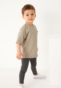 Hellgraues T-Shirt mit kurzen Ärmeln und geripptem Muster, kombiniert mit dunkelgrauen Leggings und weißen Sneakern mit roten Streifen.