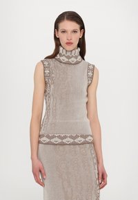 Top sans manches en tricot beige et marron avec un col montant. Présente des accents à motifs le long des épaules et de l'ourlet. Texture lisse.