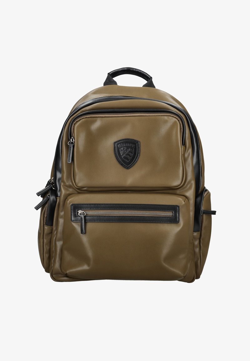 Mochila caqui fabricada con material sintético que presenta una textura suave, acentos negros, múltiples cremalleras y un logo de escudo en la parte frontal.