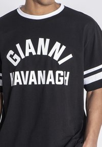 Čierne tričko s bielym textom "GIANNI KAVANAGH," s okrúhlym výstrihom a krátkymi rukávmi so bielymi pruhmi na manžetách. Z bavlneného materiálu.