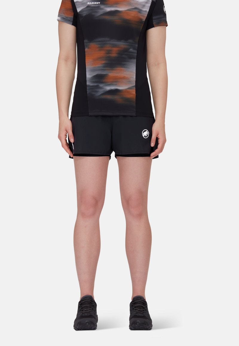 Svart atletiska shorts med en åtsittande design, kombinerat med en kortärmad topp med ett abstrakt mönster i orange och grått.