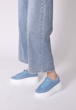 Blaue Wildledersneaker mit einem perforierten Design, weißer Plateausohle und passenden Schnürsenkeln. Getragen mit hellblauen weit geschnittenen Jeans.
