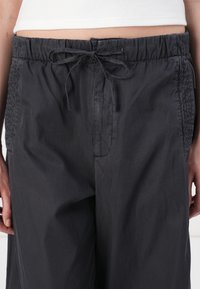 Dark gray trousers with an elastic waistband and a drawstring. Smooth texture, featuring side pockets and gathered detailing on sides.