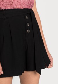 Black shorts with a tied waist, pleated design, and three dark buttons on the front. Features a smooth texture and mid-thigh length.