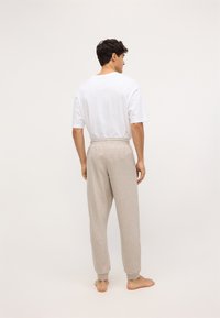 Tricou alb cu mânecă scurtă, asortat cu pantaloni de trening gri deschis, cu croială lejeră, și cu talie și manșete elastice, prezentat din spate.