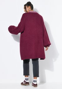 Cardigan en tricot bordeaux surdimensionné avec des manches longues et des poignets côtelés. Associé à un jean noir cropped et des baskets bordeaux.