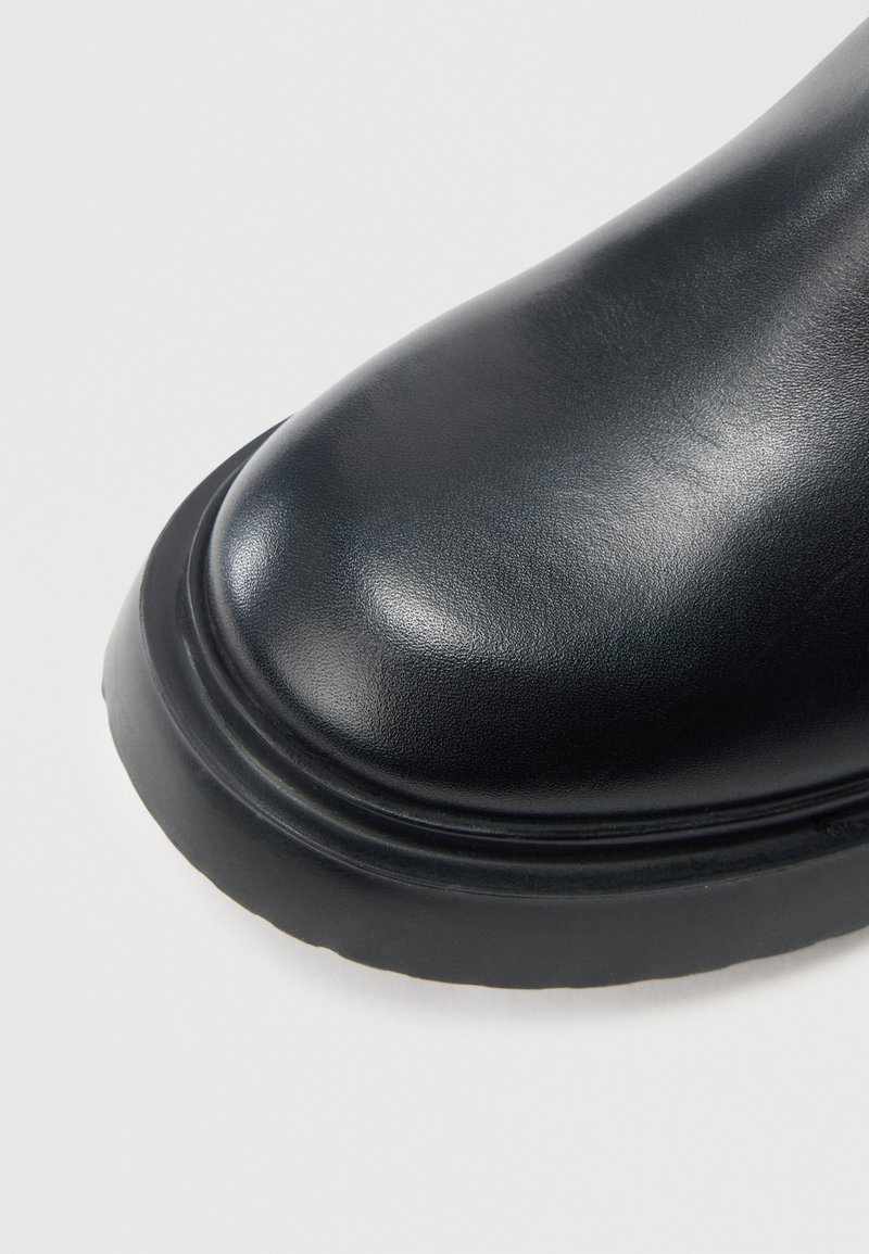 Stivale in pelle nera con punta arrotondata e texture liscia, dotato di suola definita con sottili scanalature. Design semplice e funzionale.