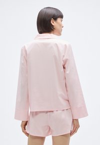 Ensemble de pyjama en coton rose comprenant un haut à manches longues avec col et un short, avec une texture lisse, présenté de dos.