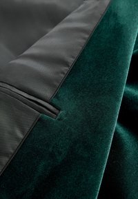 Dark green velvet fabric with a soft texture, layered alongside smooth black textile. Features a clean, modern design with stitching accents.