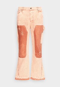 Jeans de tono durazno claro con parches grandes de color óxido oscuro en las rodillas, detalles desgastados y un bolsillo lateral para herramientas, mostrados de forma plana sobre un fondo blanco.