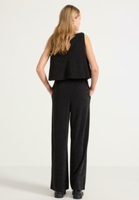 Czarny, błyszczący kombinezon z luźnym, skróconym topem i szerokimi spodniami. Teksturowana tkanina z niskim wycięciem na plecach. Odpowiedni na formalne okazje.