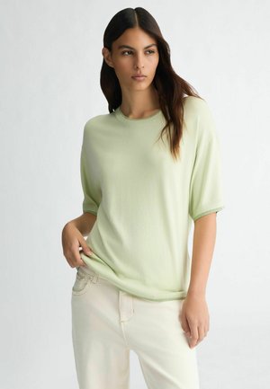 Light green short-sleeve sweater with ribbed neckline and hem, paired with cream-colored pants, displayed against a neutral background.