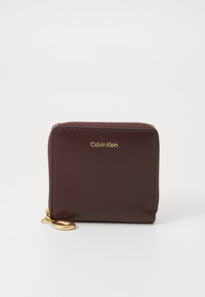 Burgundy leather wallet with gold zipper hardware and a keyring attachment. Features a smooth texture and the "Calvin Klein" logo embossed.