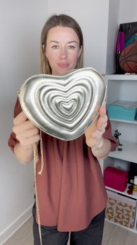 Silverfärgad hjärtformad väska med lager av hjärtmönster, en kedjesnor och en metallisk finish. Slät textur med subtila sömnadsdetaljer.