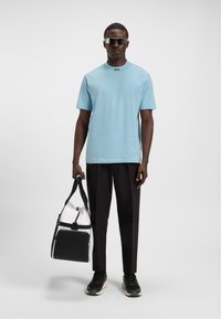 Cămașă bleu deschis cu mânecă scurtă, pantaloni negri și adidași negri. Geantă de voiaj transparentă și neagră, cu o curea neagră. Accesorii: ochelari de soare negri.