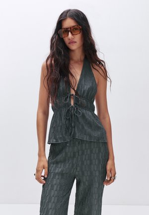 Top halter verde scuro con la parte anteriore annodata e tessuto strutturato, abbinato a pantaloni coordinati in tessuto strutturato, caratterizzati da una vestibilità rilassata.