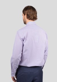 Man with light purple checkered dress shirt and navy pants, viewed from the back against a plain light gray background.