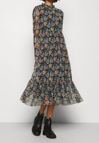 Blomstret midi kjole med lange ærmer, sort gennemsigtigt stof, med farverige blomster og blade samt en flæsekant. Bæres med sorte ankelstøvler.