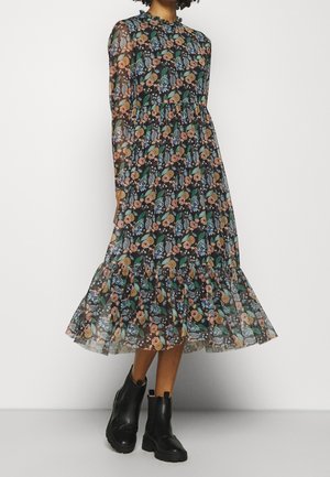 Sukienka midi w kwiatowy wzór z długimi rękawami, wykonana z czarnego przezroczystego materiału, ozdobiona kolorowymi kwiatami i liśćmi oraz falbaną przy brzegu. Noszona z czarnymi botkami za kostkę.