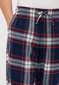 Rutete pysjamasbukser i marineblått, burgunder og hvitt. Laget av mykt stoff med elastisk midje og snor. Har sidelommer.