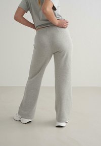 Grå sweatpants med afslappet pasform og elastisk talje, parret med en grå top med korte ærmer. Hvide sneakers synlige ved fødderne.