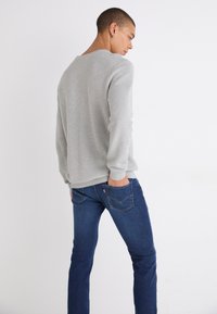 Grå strikkegenser med lange ermer og rund hals, sammen med mørkeblå jeans med baklommer og subtile sømdetaljer.