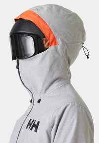 Sjezdová bunda ze světle šedé látky s texturovaným vzorem, s jasně oranžovým akcentem na kapuci a černým logem na hrudi.