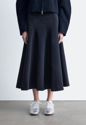 Ein marineblauer Rock in A-Linie aus weichem Stoff, kombiniert mit silbernen Sneakers. Der Rock hat eine taillierte Passform und einen ausgestellten Saum.