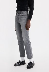 Jeans grises de cintura alta con pierna recta, que cuentan con un clásico diseño de cinco bolsillos y una sutil textura desgastada, combinados con mocasines negros.