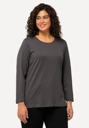 Long-sleeve dark gray shirt made of soft fabric, featuring a round neckline and a relaxed fit, displayed on a model with curly hair.