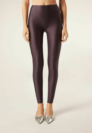 Hooggeplaatste, glanzende pruimenleggings van een gladde, rekbare stof, gecombineerd met zilveren schoenen met spitse neuzen.