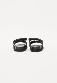 Sandali neri con design aperto, caratterizzati da due cinghie sulla parte superiore e una soletta testurizzata. Suola inferiore scura con minimi accenti hardware.