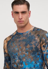 Cămașă sport cu mânecă lungă, în model tie-dye albastru și maro, realizată dintr-un material neted, cu decolteu rotund și mâneci raglan.