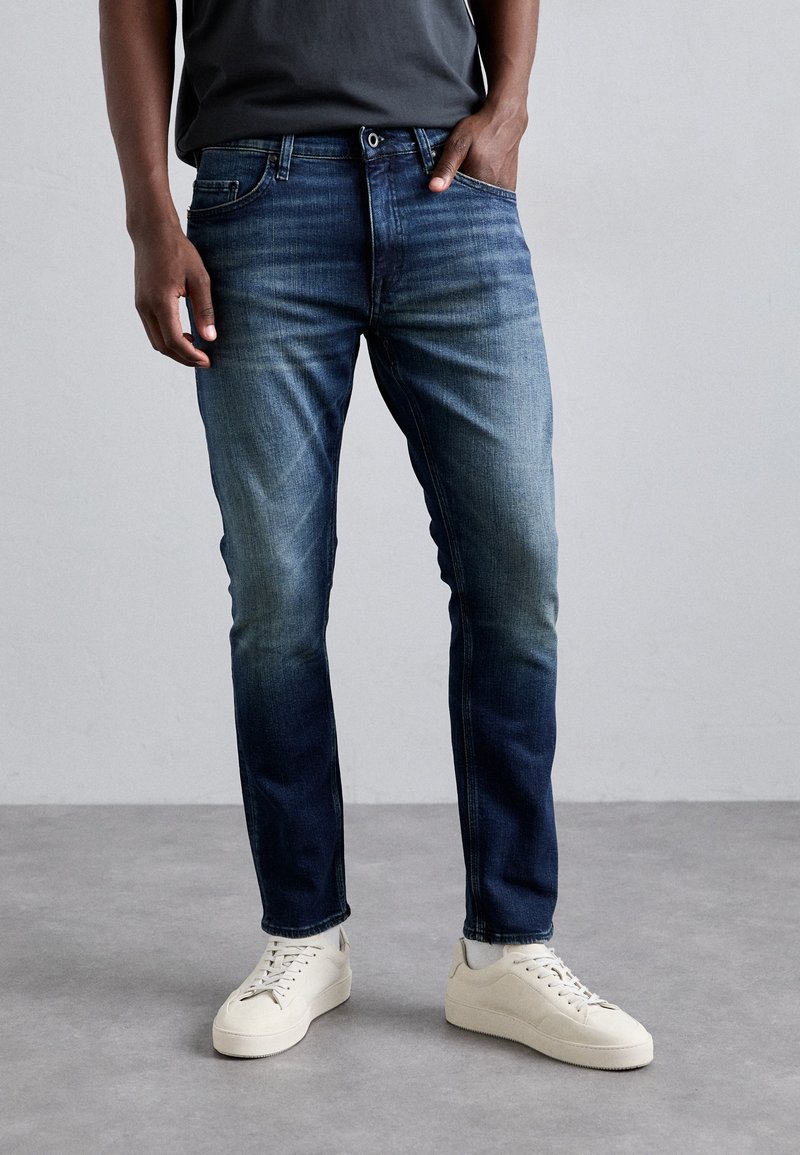 Slim fit jeans i blekt mörkblå denim, med en klassisk femfickdesign och dragkedja, tillsammans med vita sneakers.