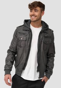 Chaqueta bomber de cuero en gris oscuro con una capucha gris extraíble, múltiples bolsillos con cremallera y puños acanalados. Textura suave, diseño elegante.